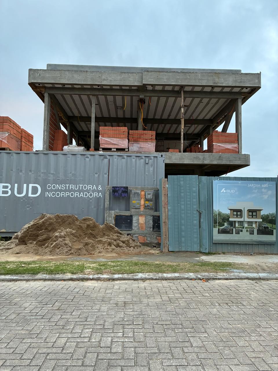 Obra em outubro de 2026 — vista frontal da fachada, com tapume e contêiner da BUD